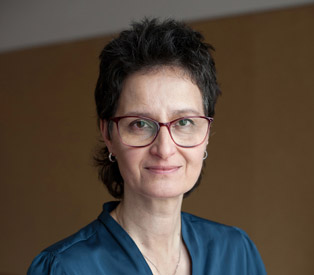 Rabea Wienholt, freundlich blickend, in einer blauen Bluse vor einem schlichten braunen Hintergrund.
